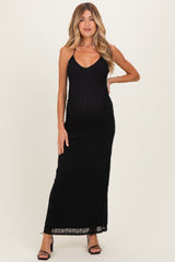 woman wearing a black maternity maxi dress with a v-neck and spaghetti straps, gently accentuating her baby bump