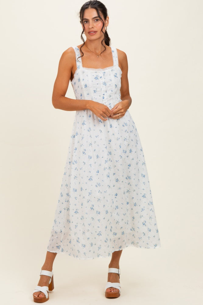 woman wearing a white midi dress with blue floral print and square neckline, standing with hands clasped