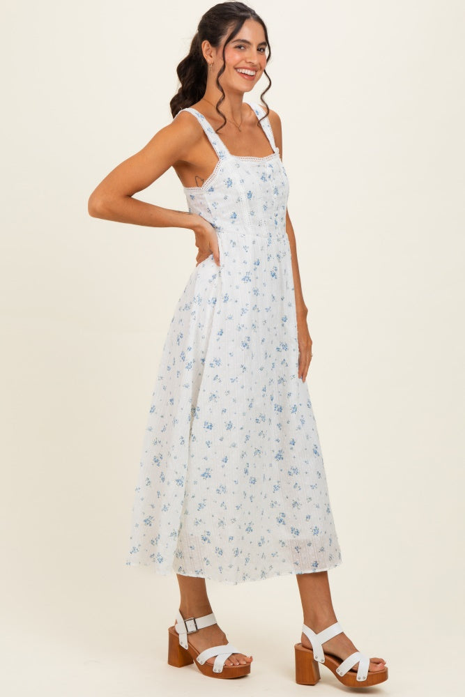 woman wearing a white floral midi dress with blue accents and a fitted bodice, paired with white heeled sandals