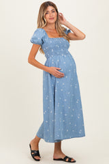 woman wearing a blue denim maternity maxi dress with puff sleeves and floral pattern, holding her baby bump
