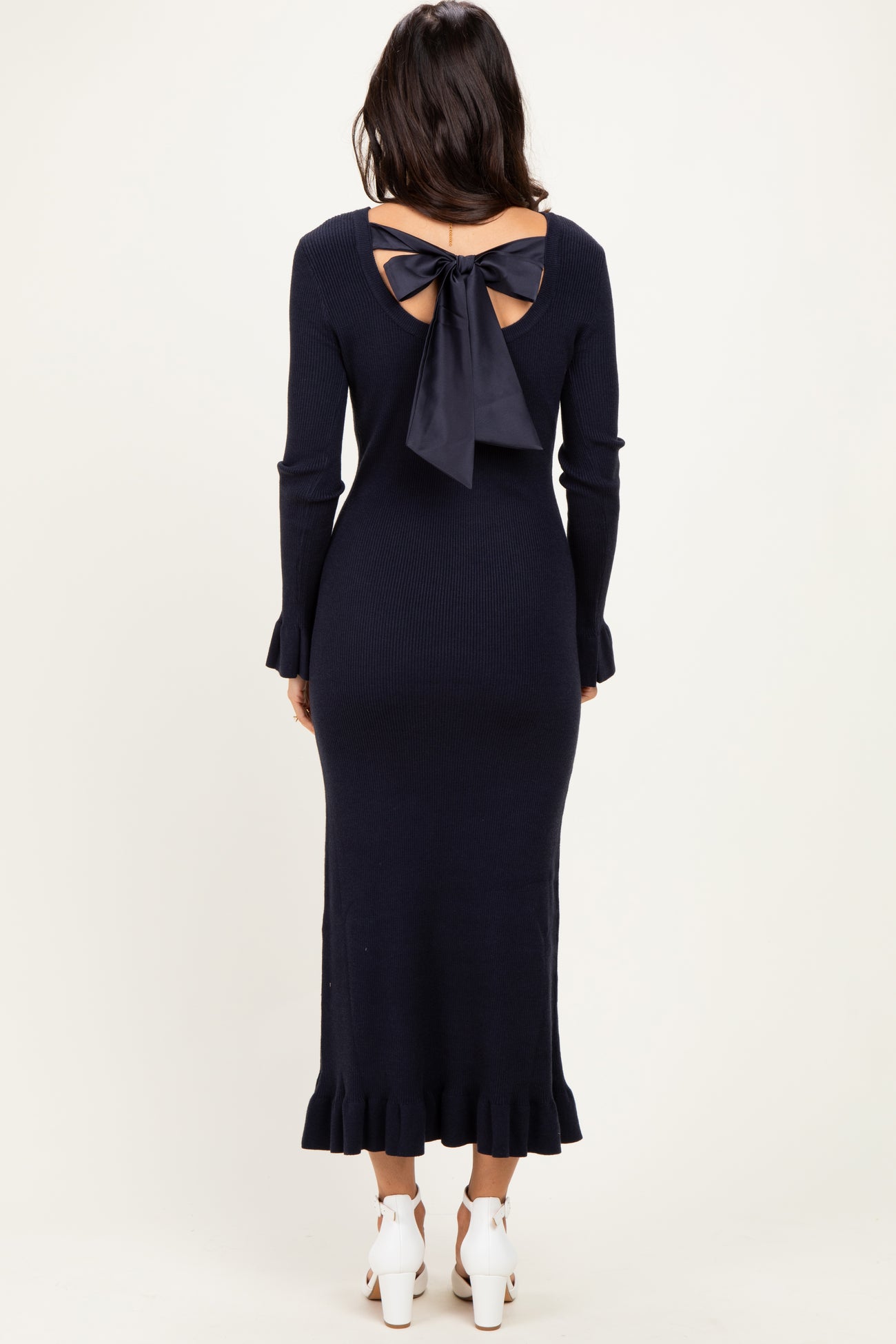 woman wearing a navy blue ribbed long sleeve dress with a back bow detail and ruffled hemline
