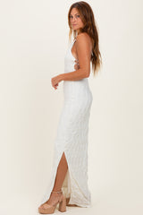 woman wearing a white fitted maxi dress with side slits and a textured fabric, standing in profile and wearing high heels