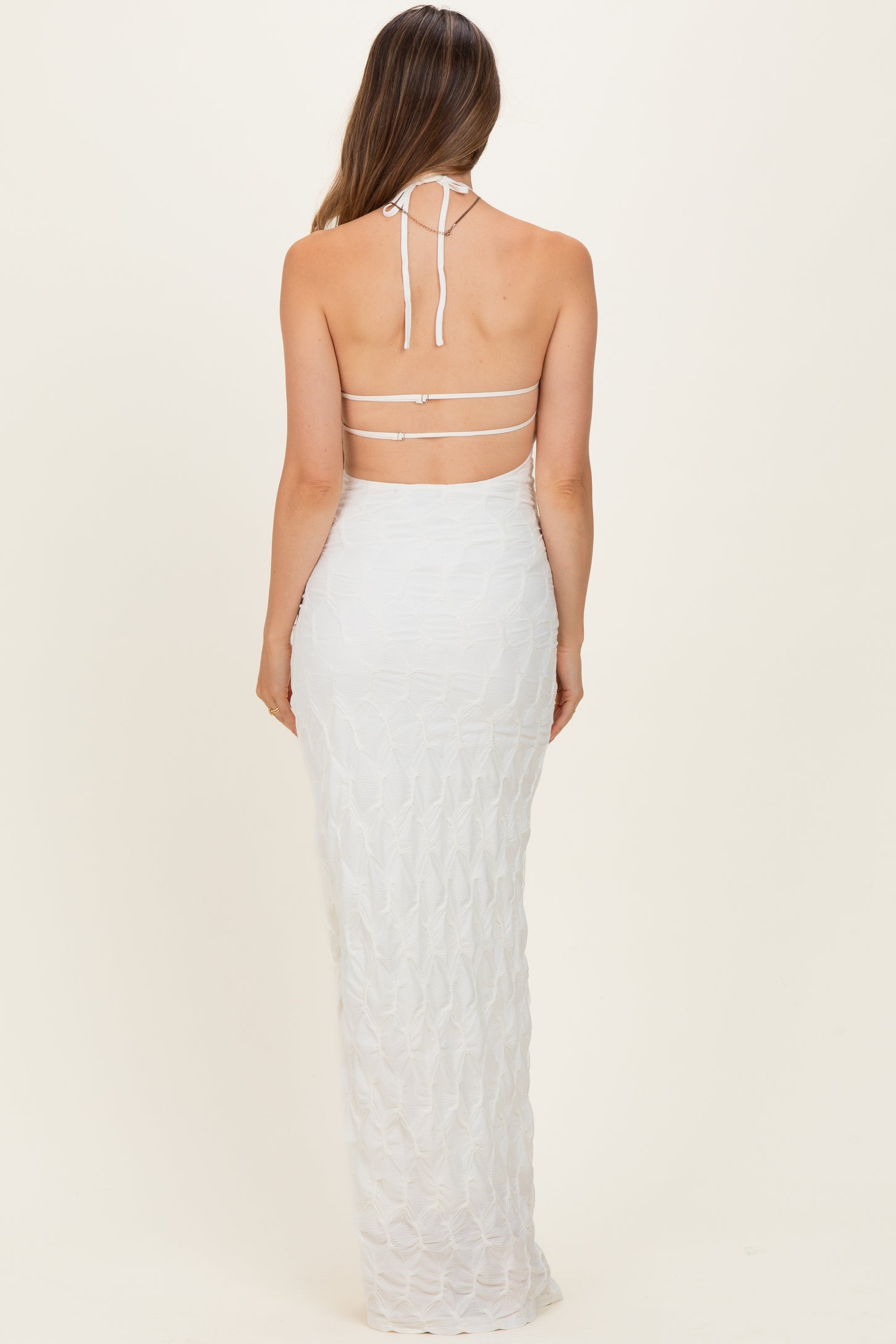 woman wearing a white halter neck maternity dress with a fitted silhouette and strappy back details
