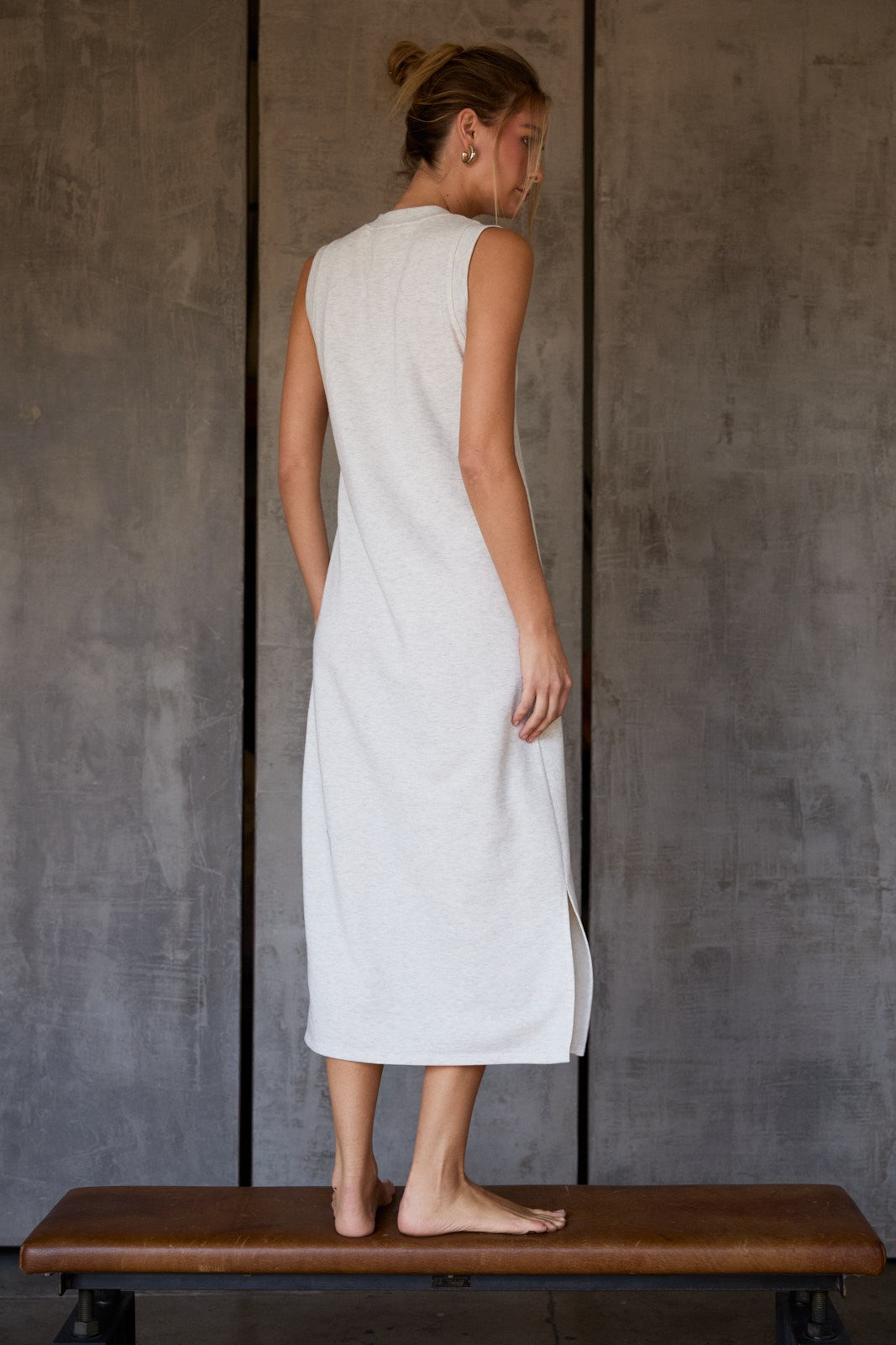 woman wearing a gray sleeveless maxi dress with a side slit, standing on a bench with a concrete background