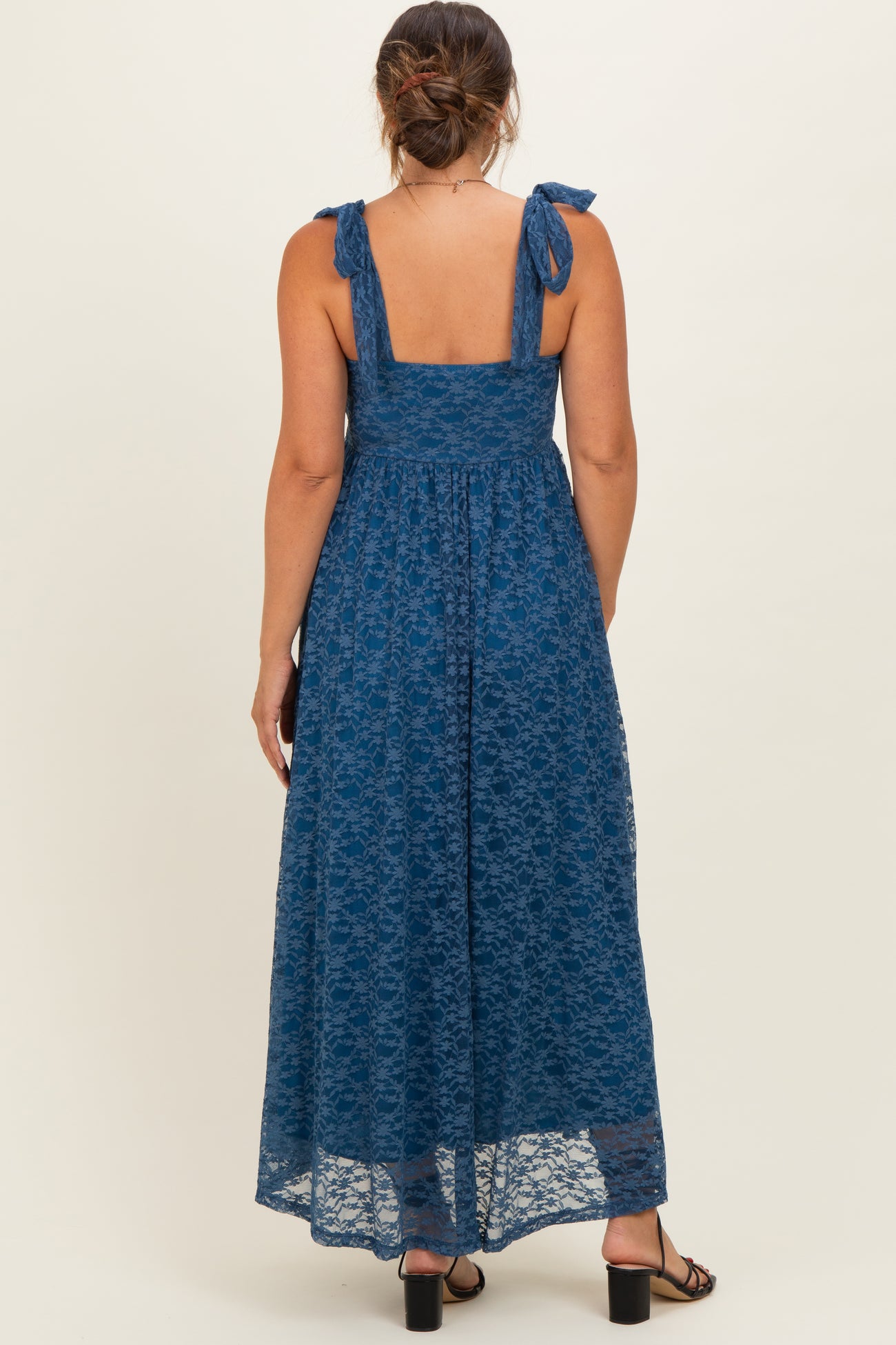 woman wearing a dark teal lace maternity maxi dress with tie shoulder straps and a flowing skirt, seen from the back