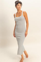 woman wearing a black and white striped spaghetti strap maxi dress, standing barefoot against a neutral background