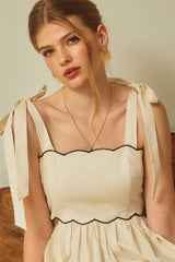 woman wearing a cream-colored sleeveless dress with scalloped edges and bow tie straps