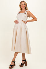 woman wearing a beige maternity dress with scalloped edges and tie straps, showcasing her baby bump, paired with black platform sandals