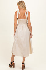 woman wearing a cream maternity dress with tie straps and a smocked back, showcasing her baby bump