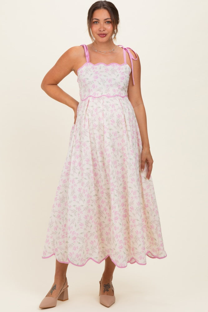woman wearing a pink floral maternity dress with scalloped edges and tie straps, showing a baby bump