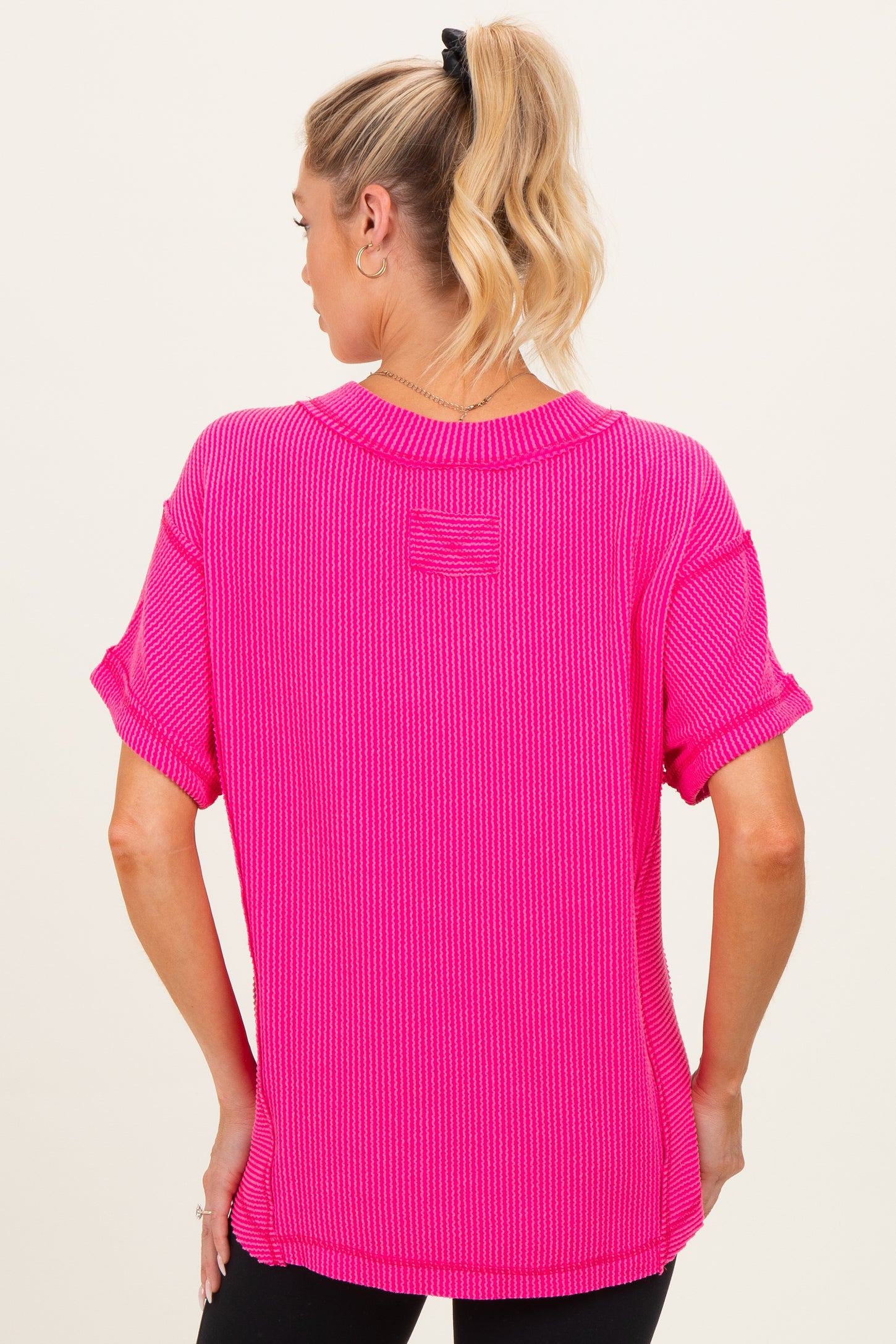 woman wearing a bright pink ribbed maternity top with rolled sleeves and a relaxed fit, showing her baby bump