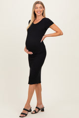 woman wearing a black ribbed maternity dress and cradling her baby bump