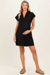 woman wearing a black maternity polo dress with a v-neck and short sleeves, holding her baby bump
