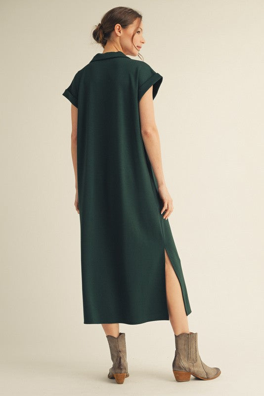 woman wearing a dark green cap sleeve maxi dress with side slit and gray ankle boots, posed from the back