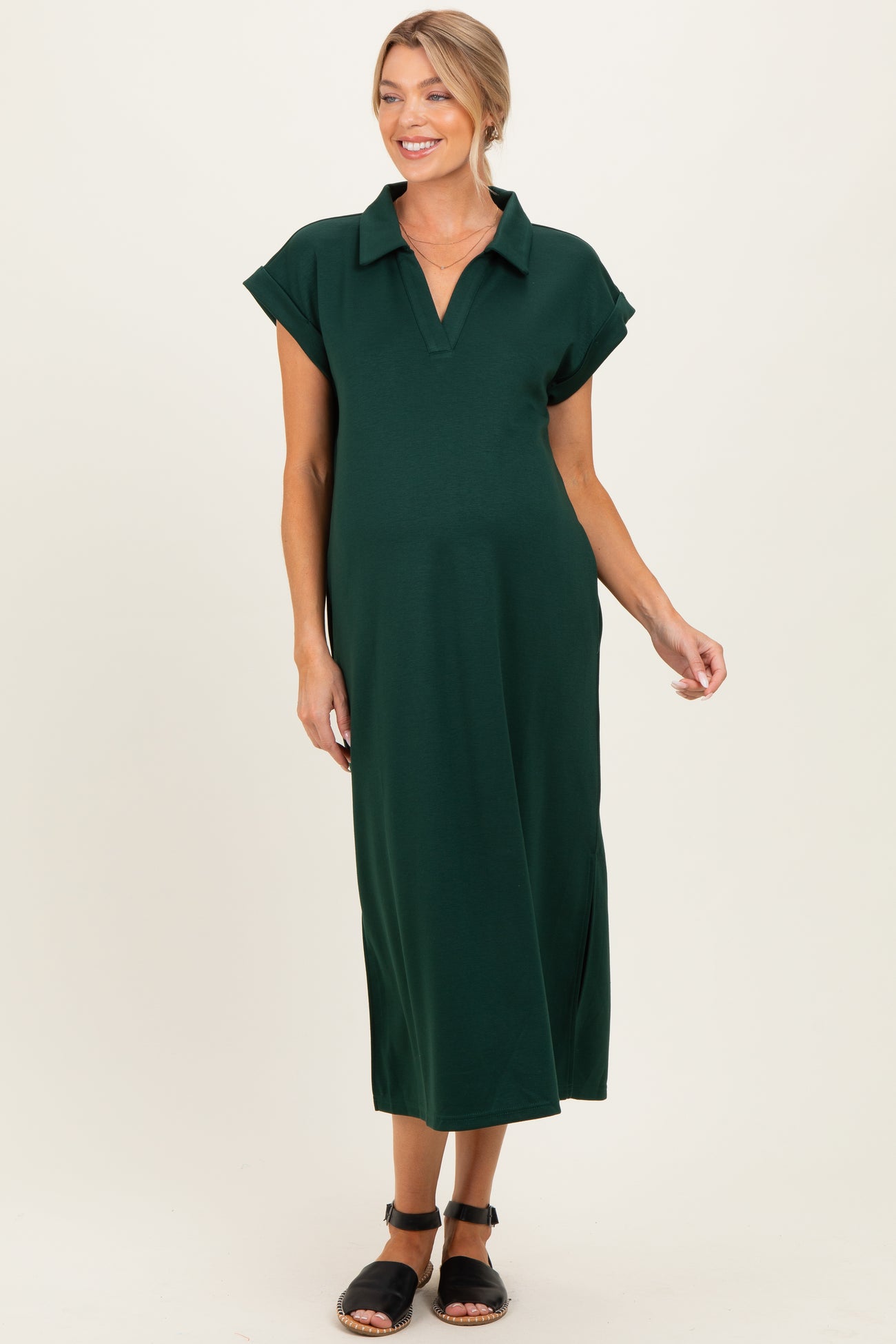 woman wearing a dark green maternity polo dress with short sleeves and side slits, showing her baby bump