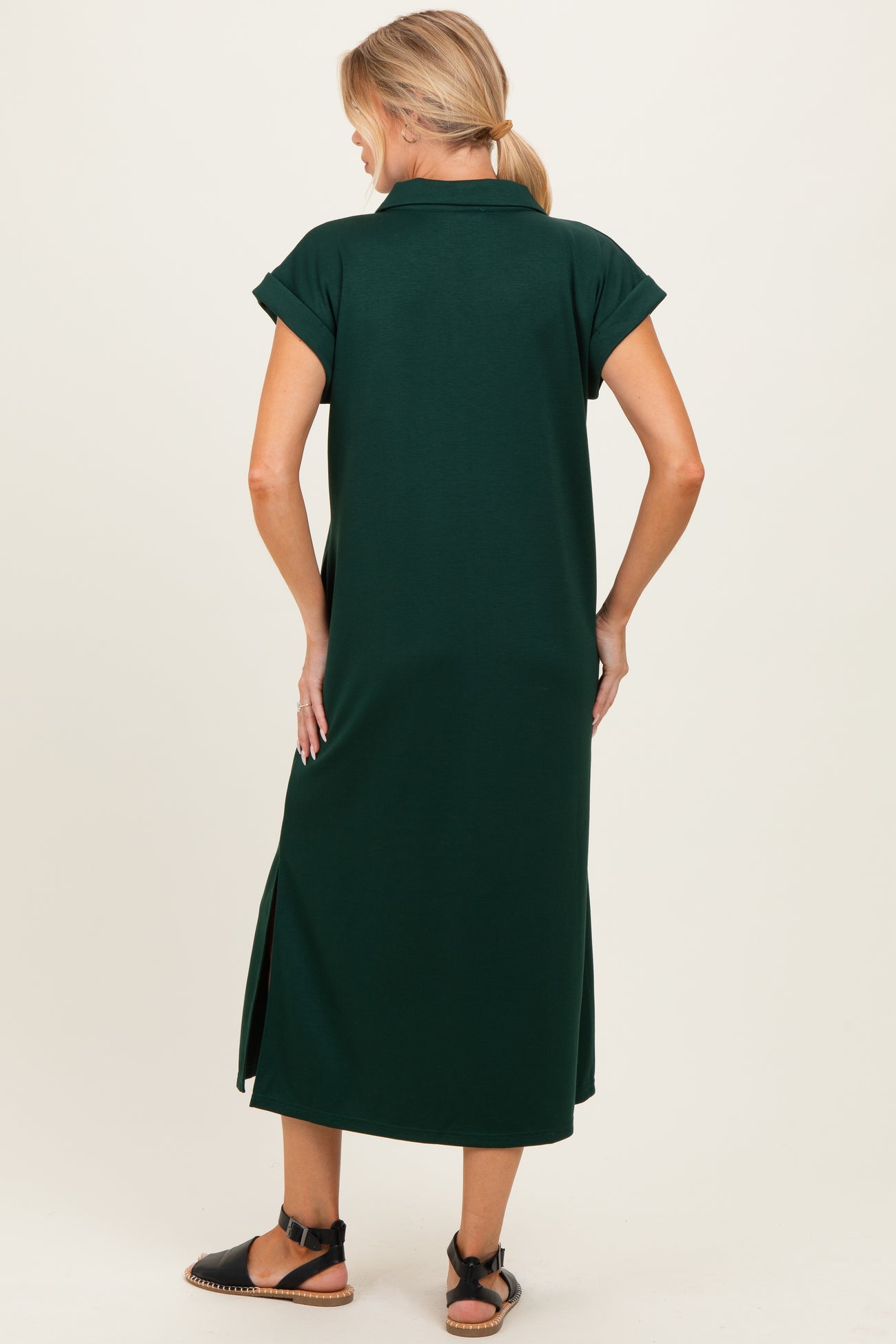 woman wearing a dark green maternity dress with short sleeves and side slits, showing the back view