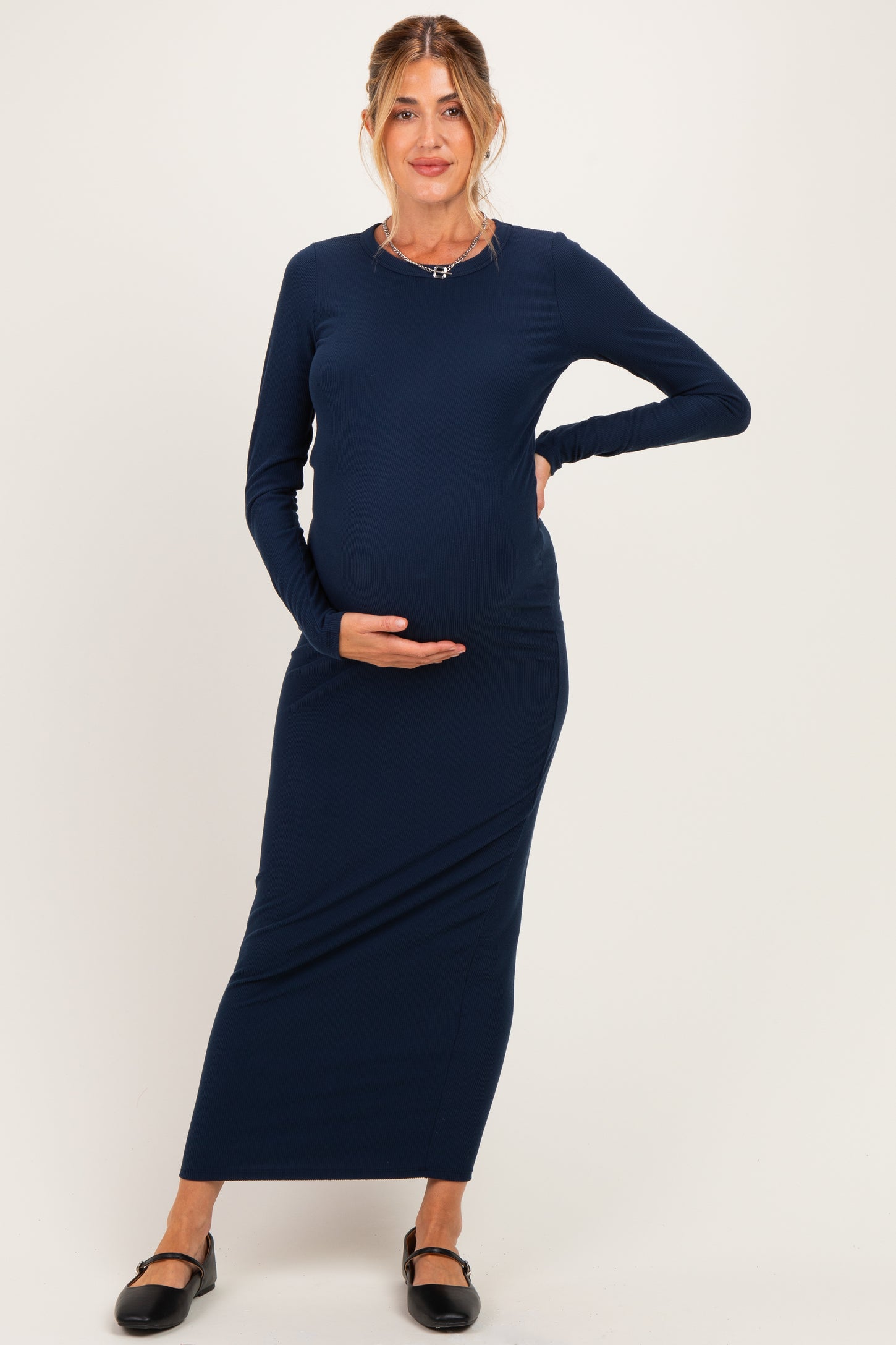 woman wearing a navy blue long sleeve maternity dress, gently cradling her baby bump