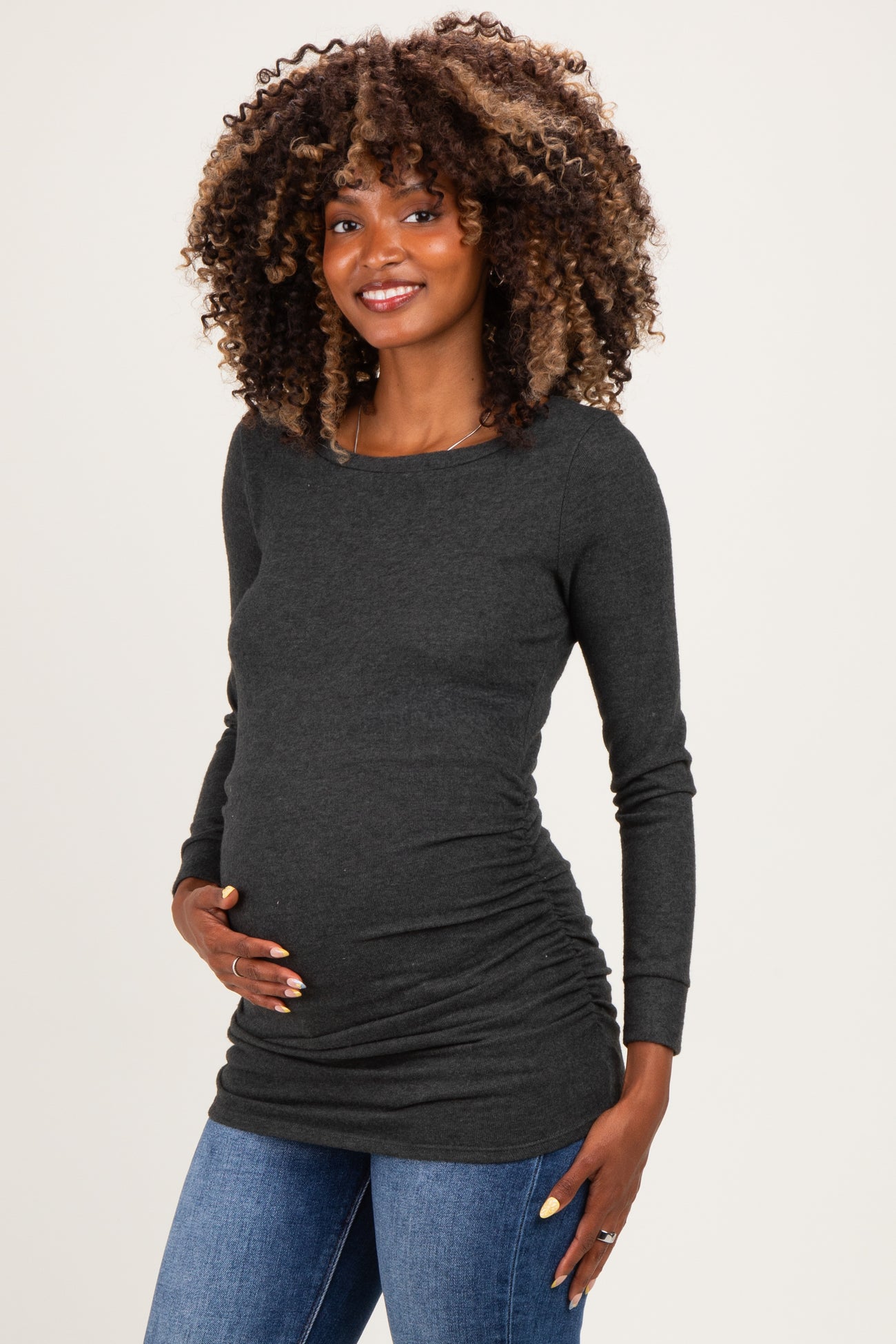 woman wearing a dark gray long sleeve maternity top, highlighting her baby bump while posing with one hand on her belly