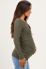 woman wearing a dark green long sleeve maternity top with gathered sides and a visible baby bump