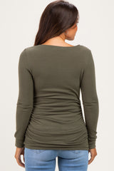 woman wearing an olive green long sleeve maternity top with side ruching, seen from the back