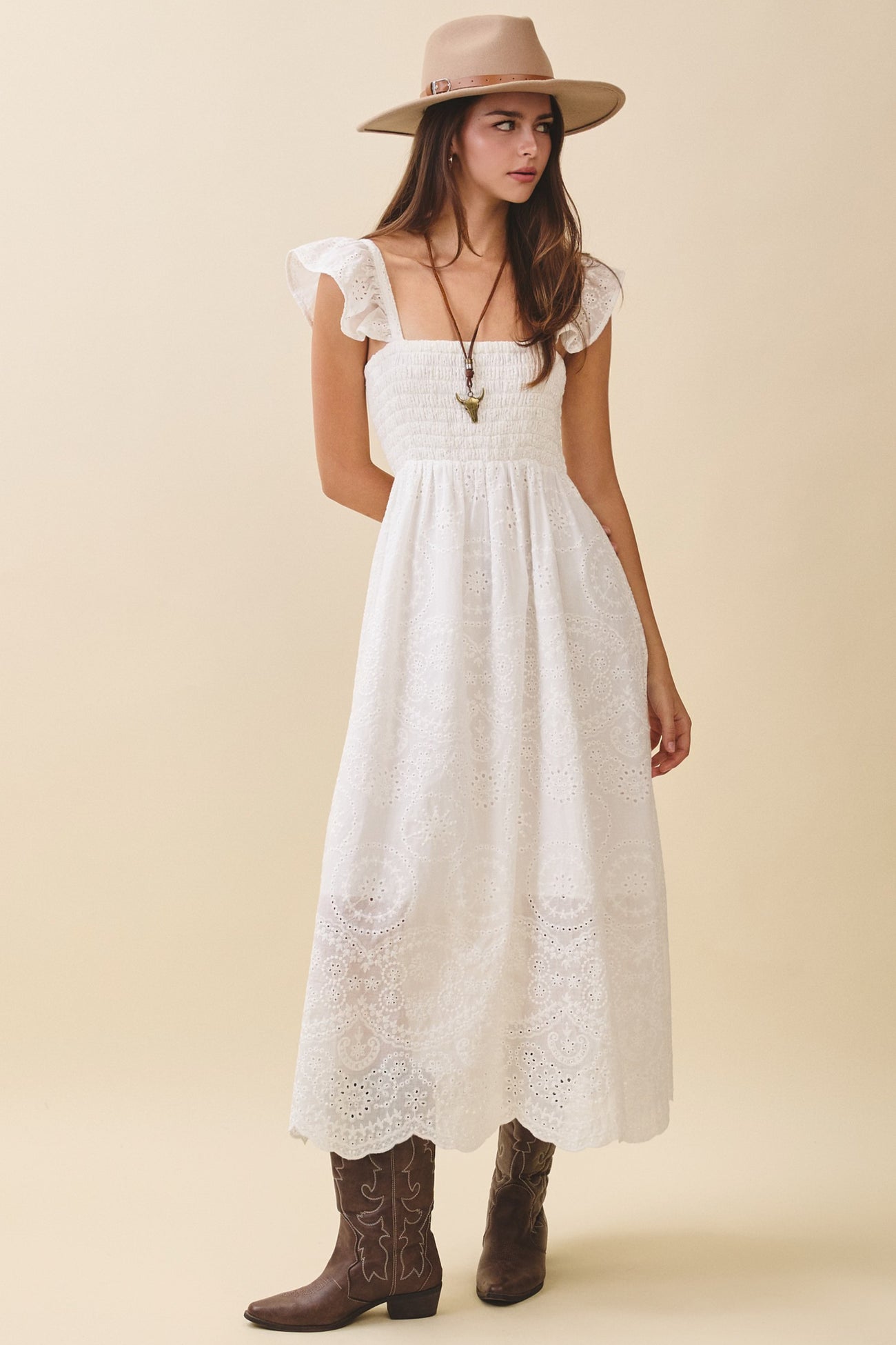 woman wearing a white maxi dress with smocking and flutter sleeves, paired with a wide-brimmed hat and brown cowboy boots