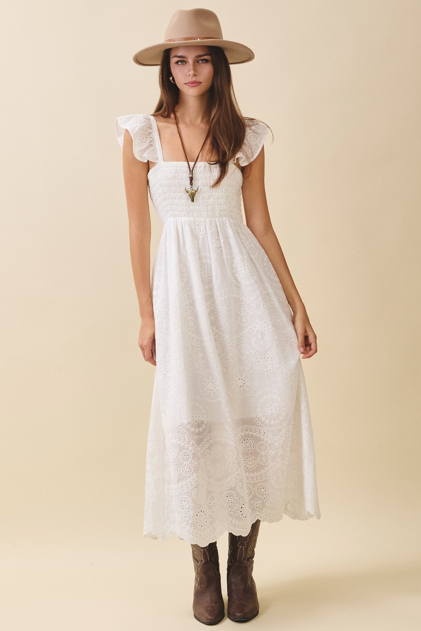 woman wearing a white maxi dress with ruffle sleeves and embroidered details, paired with a wide-brimmed hat and brown boots