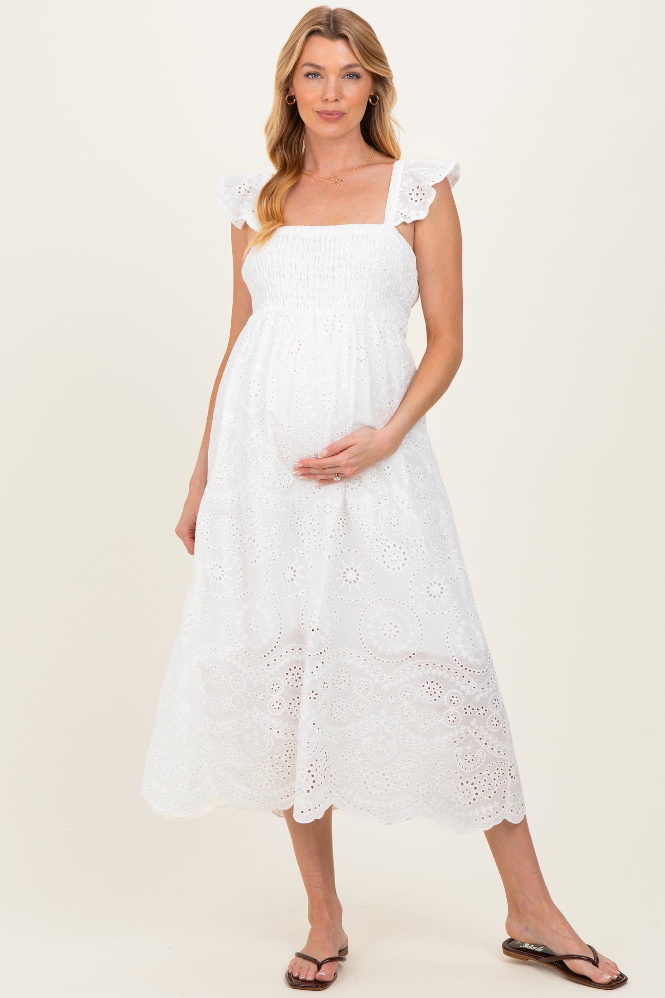 woman wearing a white maternity midi dress with ruffled sleeves and a smocked bodice, cradling her baby bump