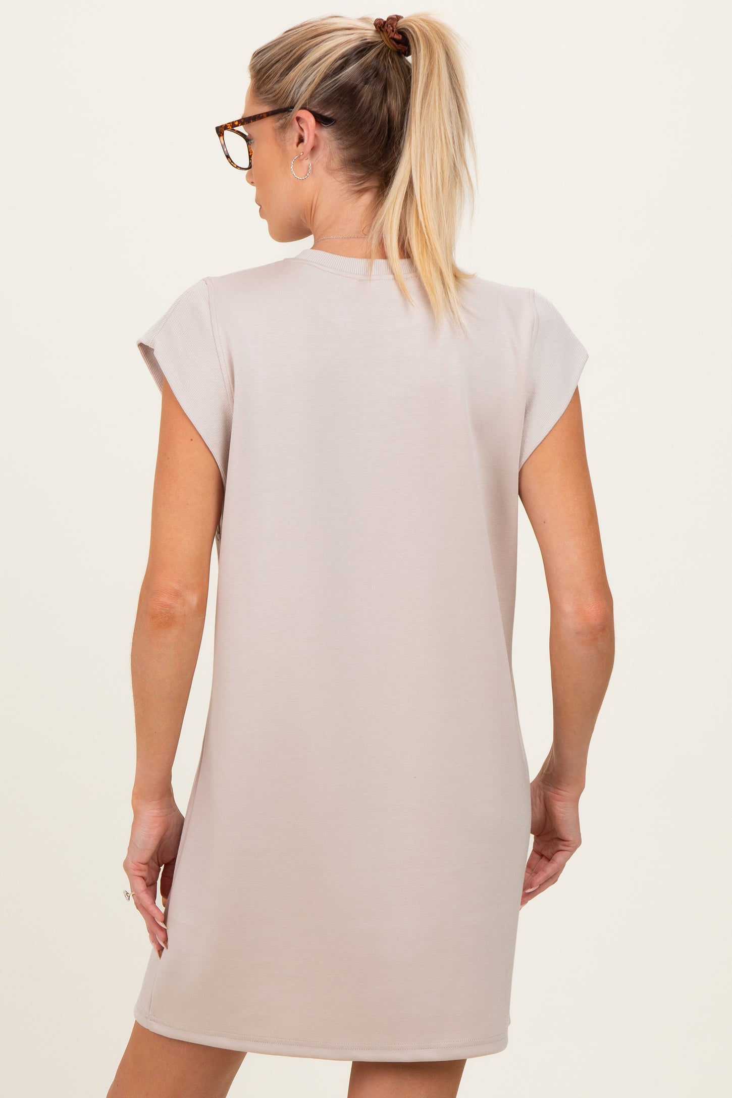 woman wearing a light beige maternity dress with cap sleeves and a relaxed fit, showing her back
