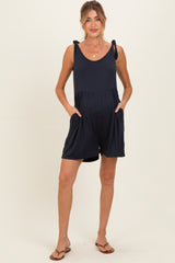 woman wearing a navy blue maternity romper with adjustable tie straps and side pockets, highlighting her baby bump