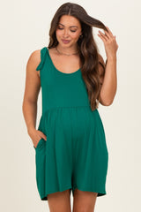 woman wearing a green maternity romper with adjustable shoulder ties and pockets, showing her baby bump
