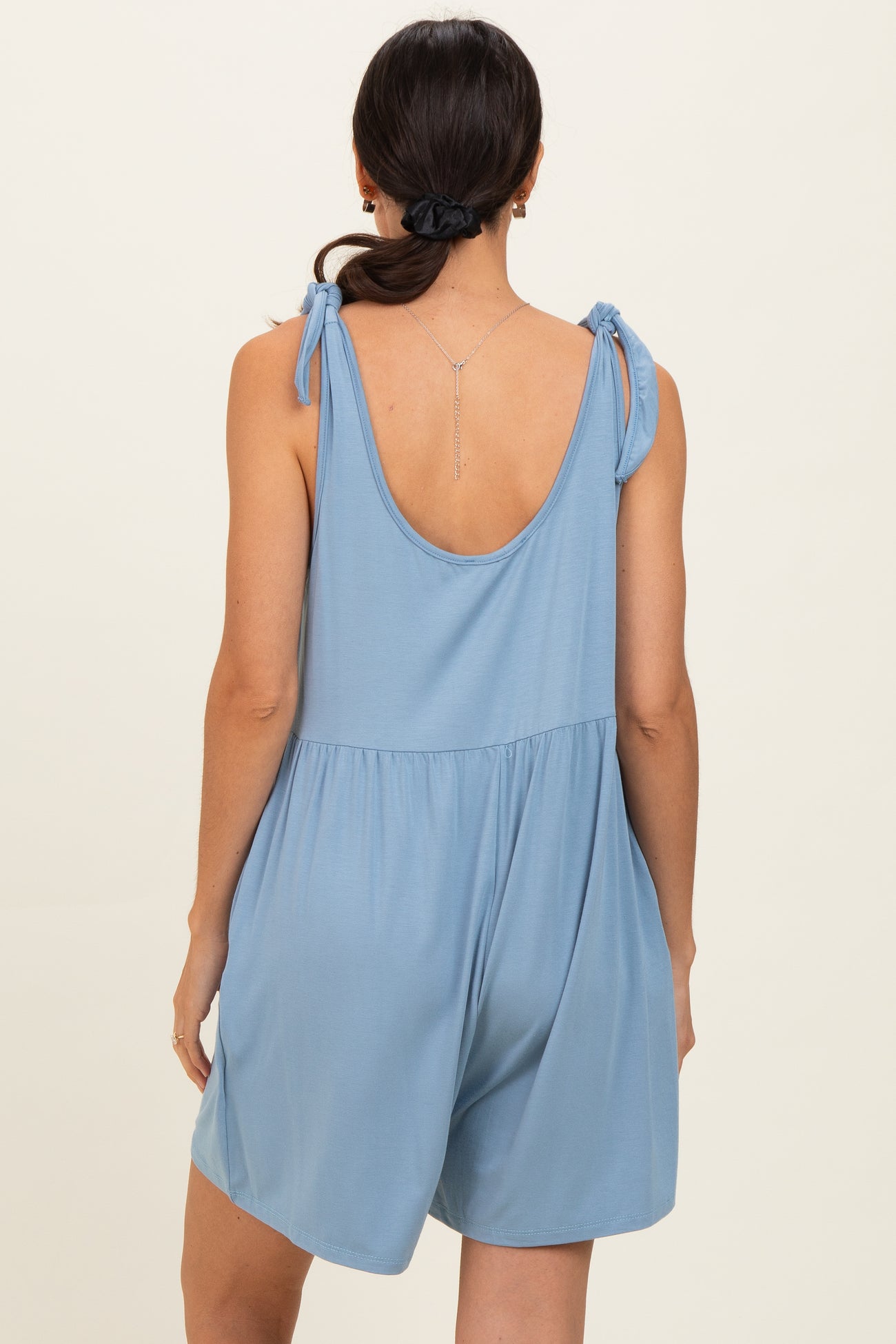 woman wearing a light blue sleeveless romper with tie details on the shoulders and a relaxed fit