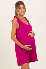 woman wearing a fuchsia maternity romper with tie straps, gently cradling her baby bump