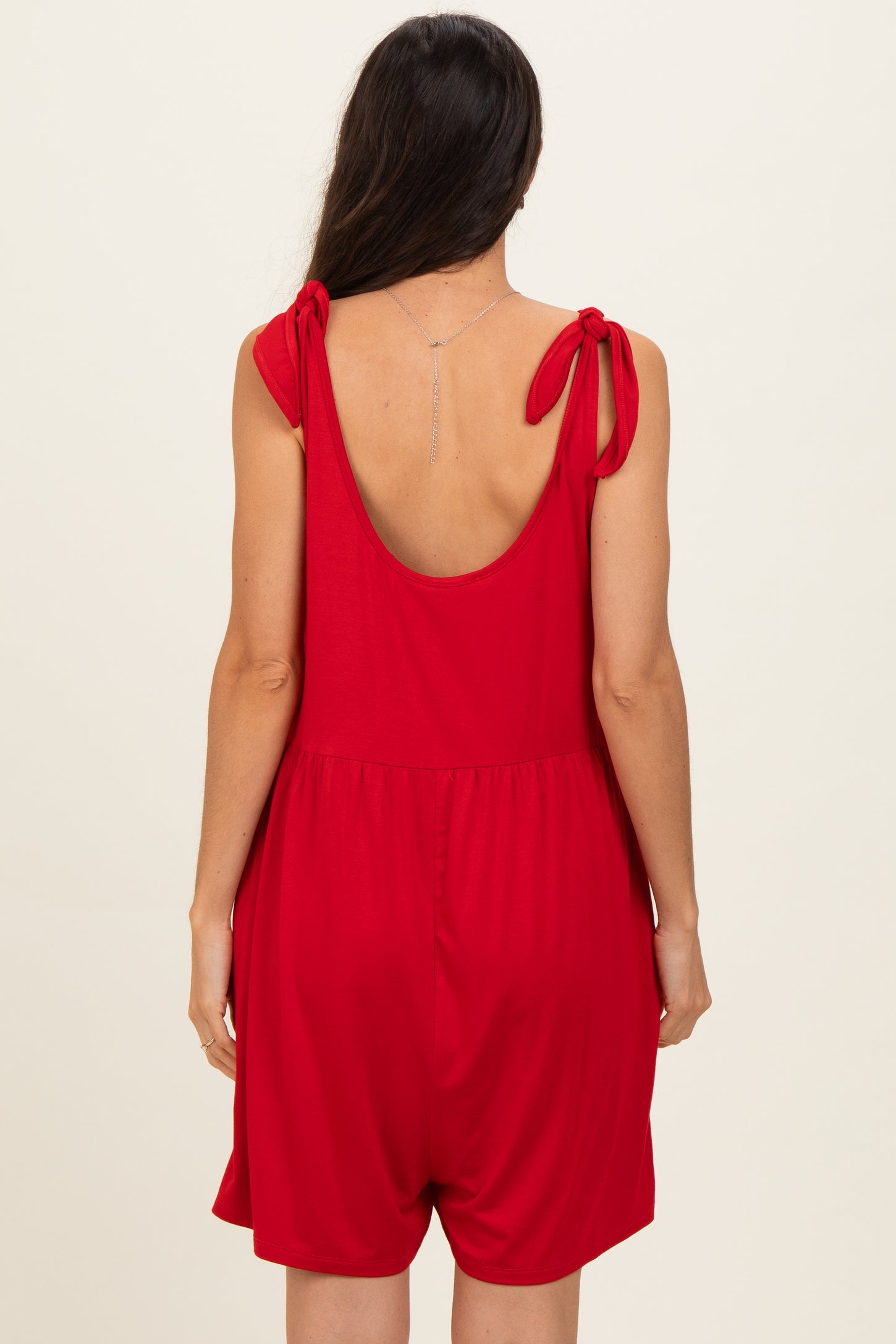 woman wearing a red sleeveless romper with tied shoulder straps, viewed from the back