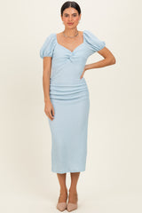 woman wearing a light blue puff sleeve midi dress with a knot detail and ruched skirt
