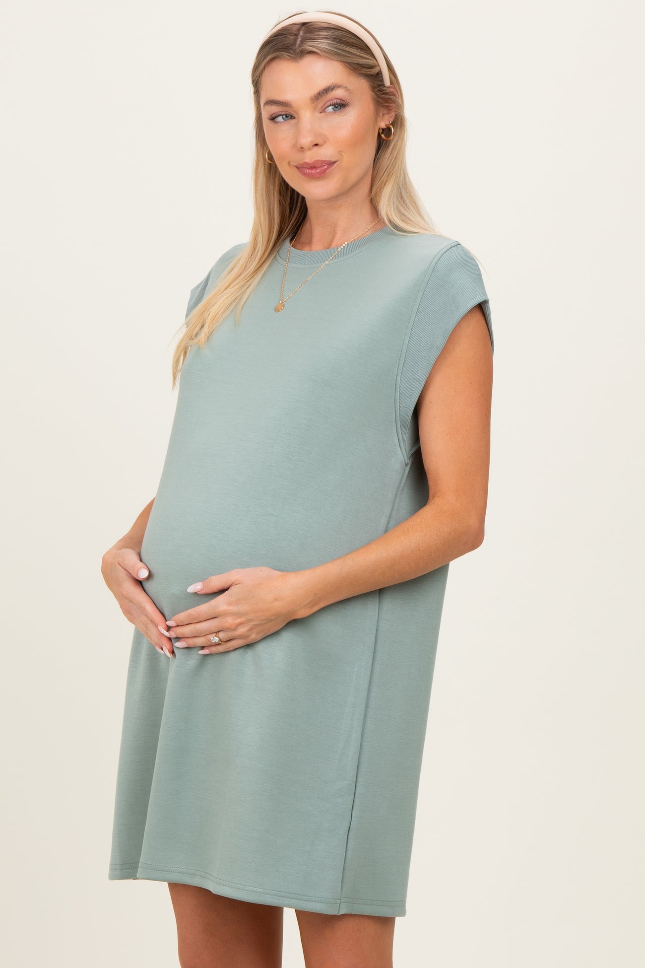 woman wearing a green short sleeve maternity dress and cradling her baby bump