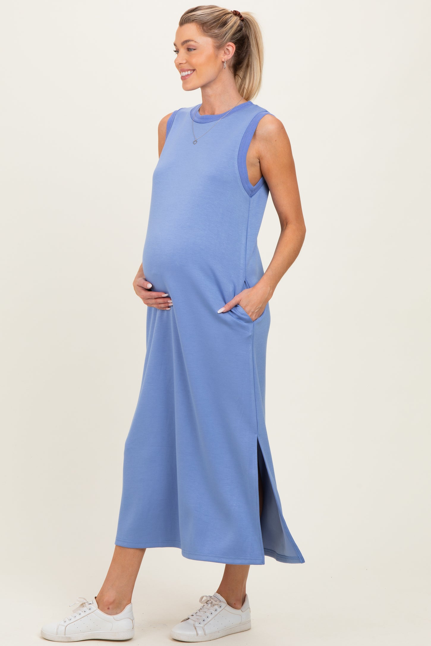 woman wearing a light blue maternity maxi dress with pockets and side slits, holding her baby bump