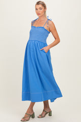 woman wearing a bright blue maternity maxi dress with smocked bodice and adjustable tie straps, showing baby bump