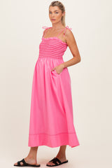 woman wearing a pink smocked maternity dress with adjustable straps and pockets