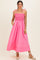 woman wearing a bright pink maxi dress with a smocked bodice and tie straps, posing with hands in pockets