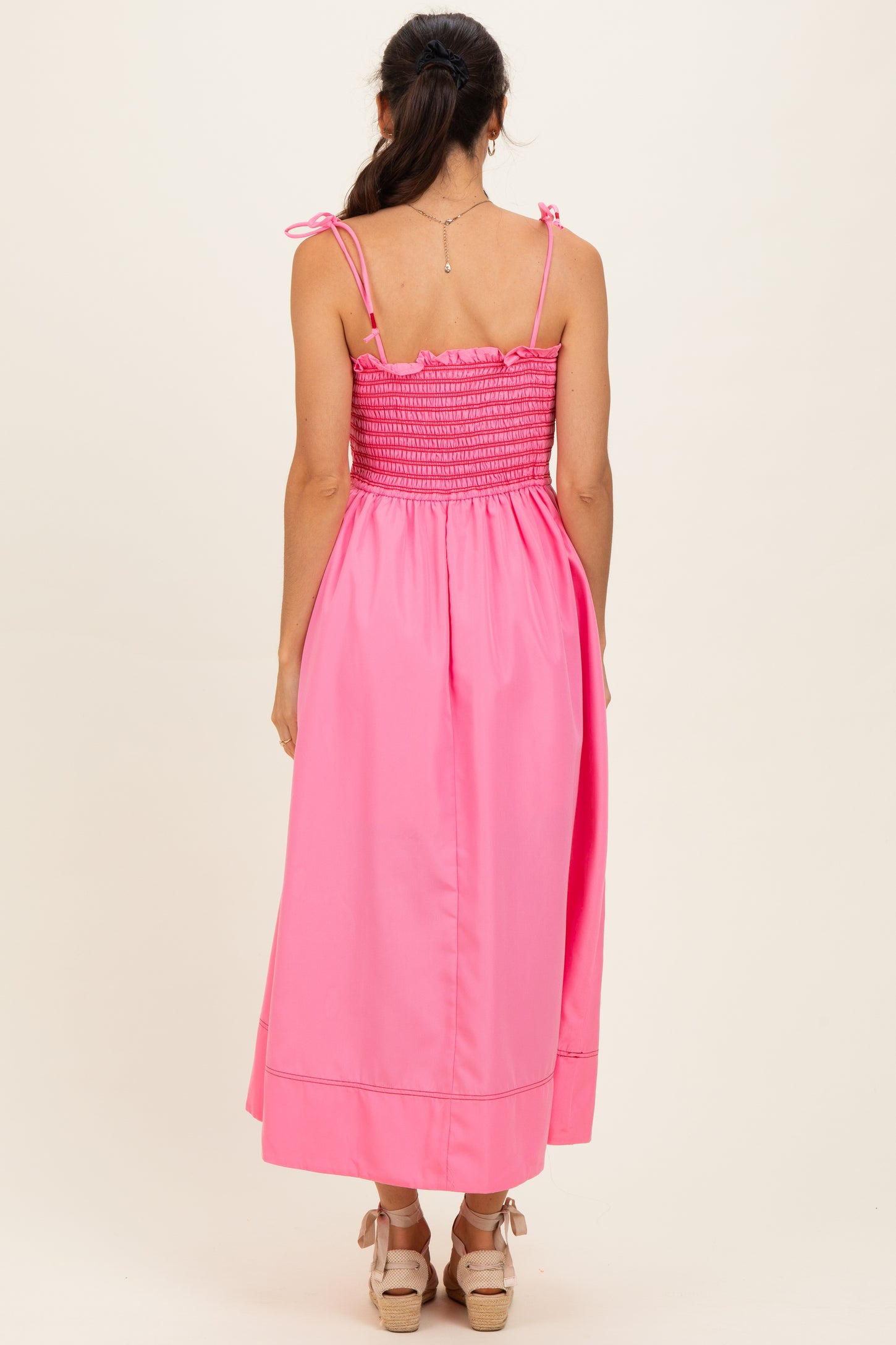 woman wearing a bright pink backless maxi dress with smocking detail and adjustable straps
