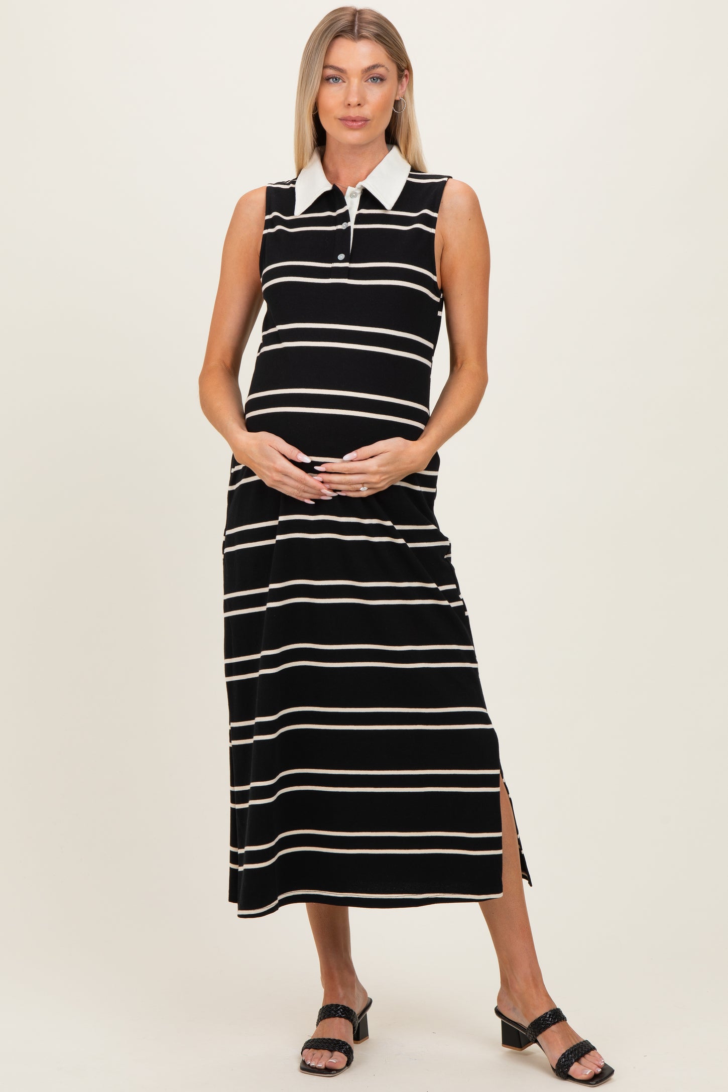 woman wearing a black and white striped maternity maxi dress with a collar and side slit, holding her baby bump