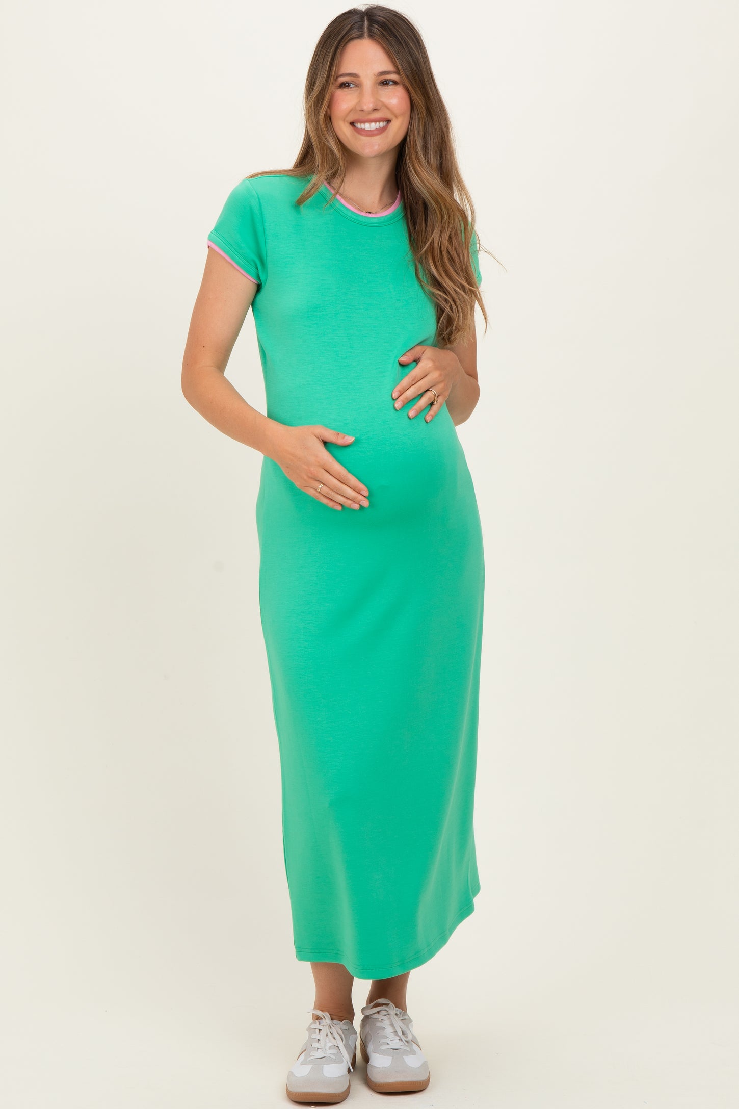 woman wearing a green maternity maxi dress with pink trim and holding her baby bump