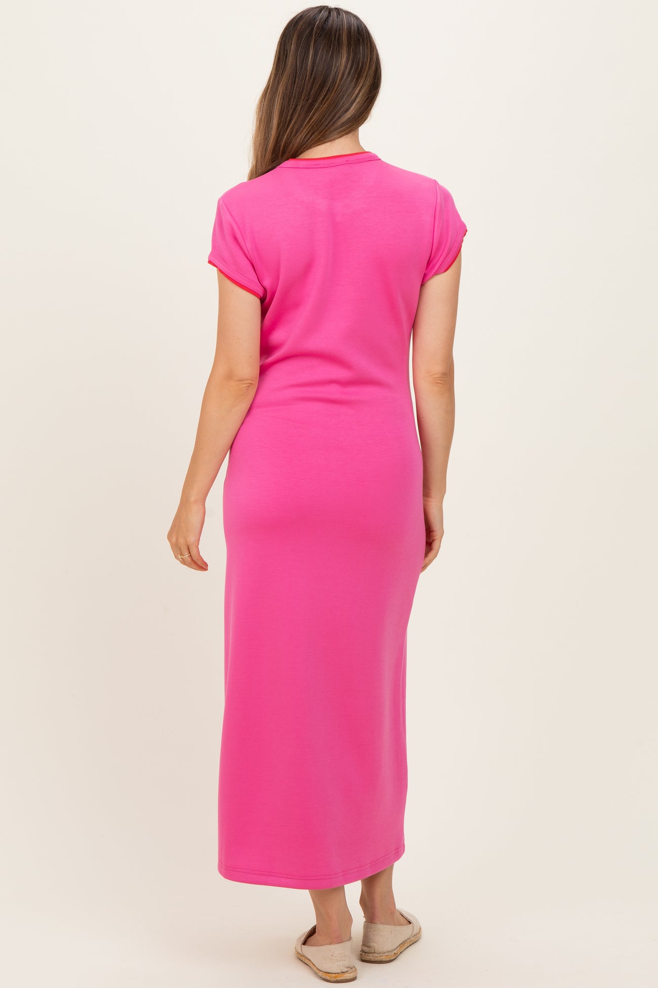 woman wearing a bright pink maternity maxi dress with short sleeves and a fitted silhouette