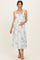 woman wearing a white floral maternity dress with smocked bodice and tie straps, gently holding her baby bump
