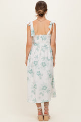 woman wearing a light blue and white floral maternity maxi dress with tie straps and a smocked bodice, showing a baby bump