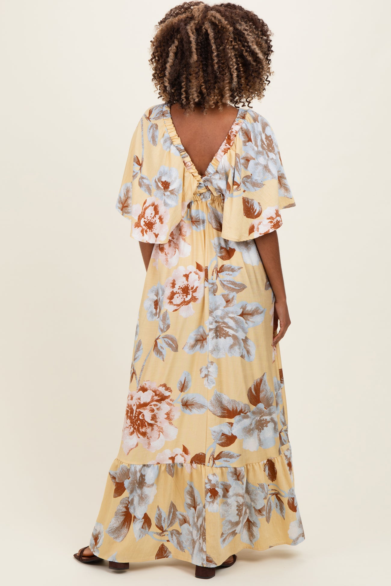 woman wearing a yellow floral maternity maxi dress with flutter sleeves and a ruffled back detail