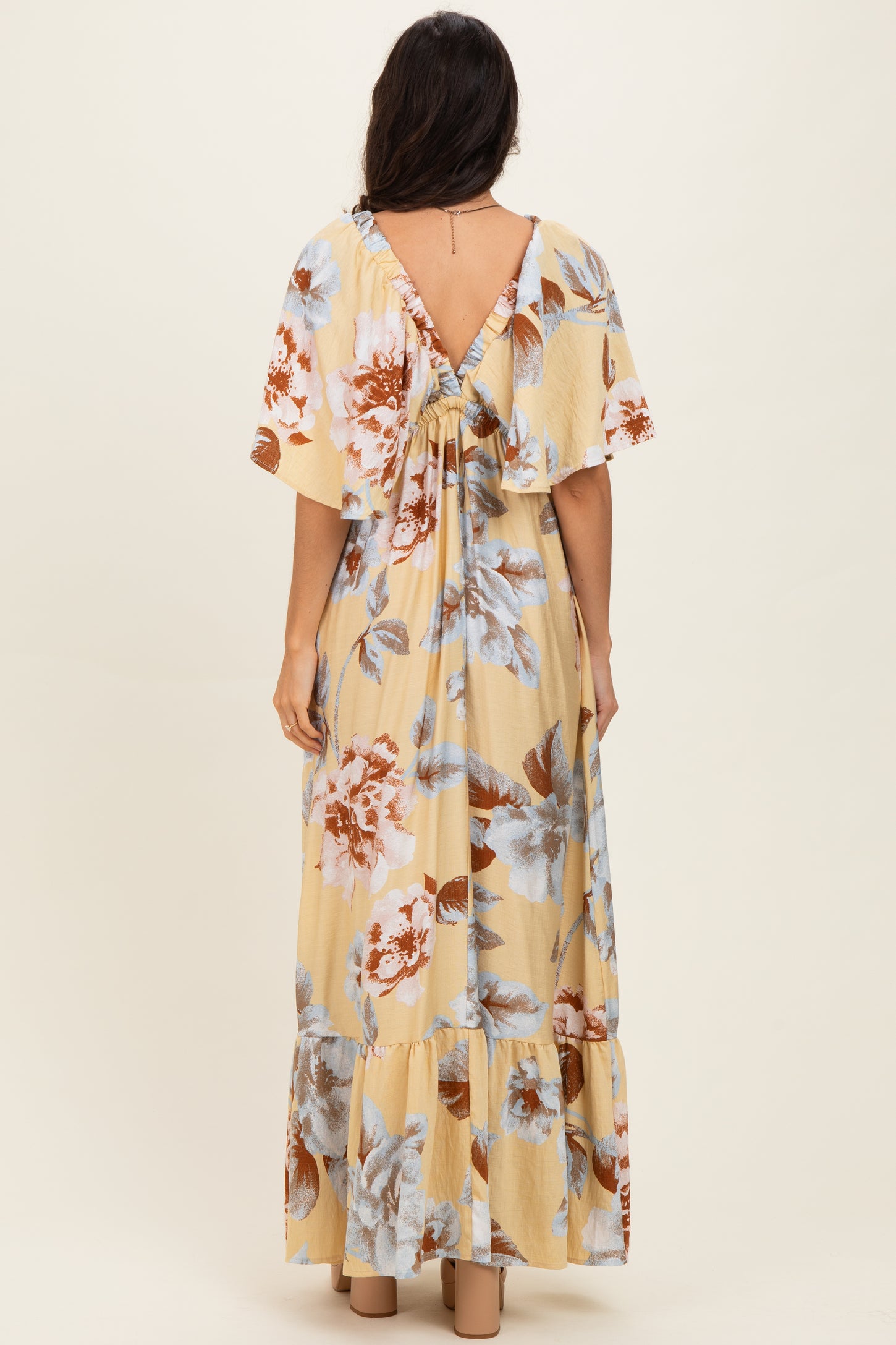 woman wearing a yellow floral maxi dress with short sleeves and a tie-back detail, viewed from the back