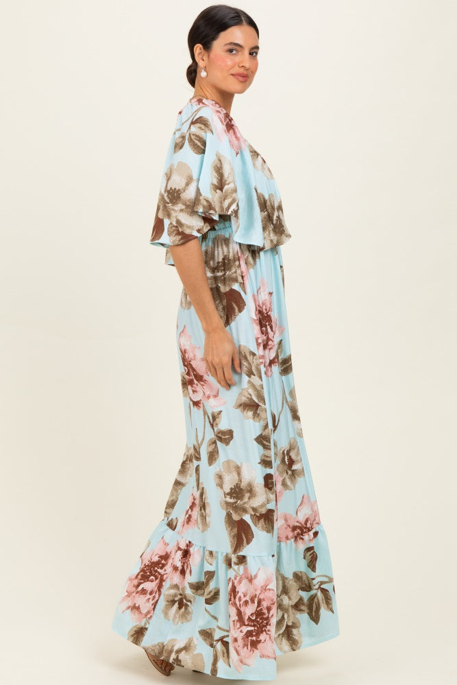 woman wearing a light blue maxi dress with large floral prints in pink and brown, featuring short sleeves and a tiered bottom