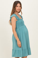 woman wearing a teal maternity dress with ruffle sleeves and a smocked bodice, showcasing her baby bump