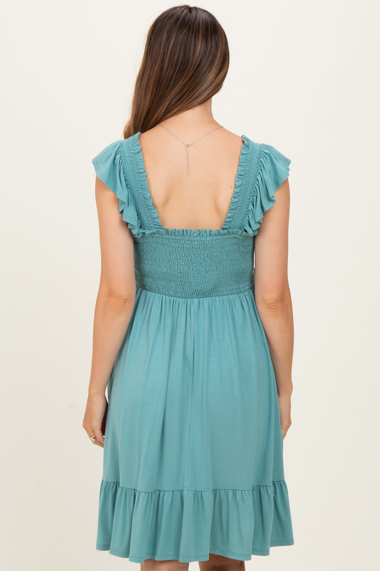 woman wearing a teal maternity dress with ruffled sleeves and a smocked back, showcasing a flowing skirt